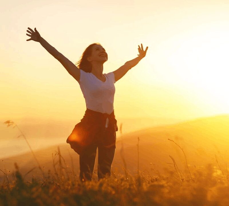 A woman standing in the grass with her arms outstretched.