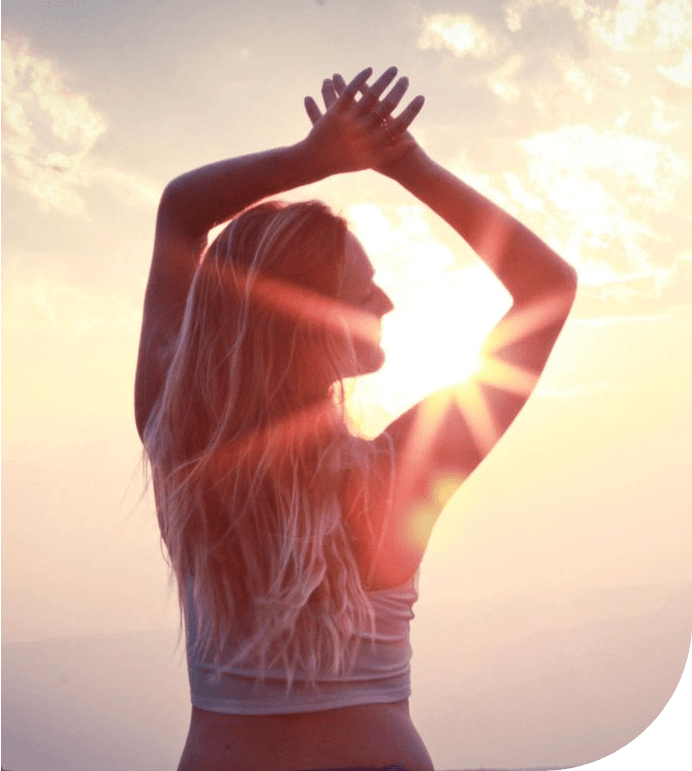 A woman is standing in the sunlight with her hands up.